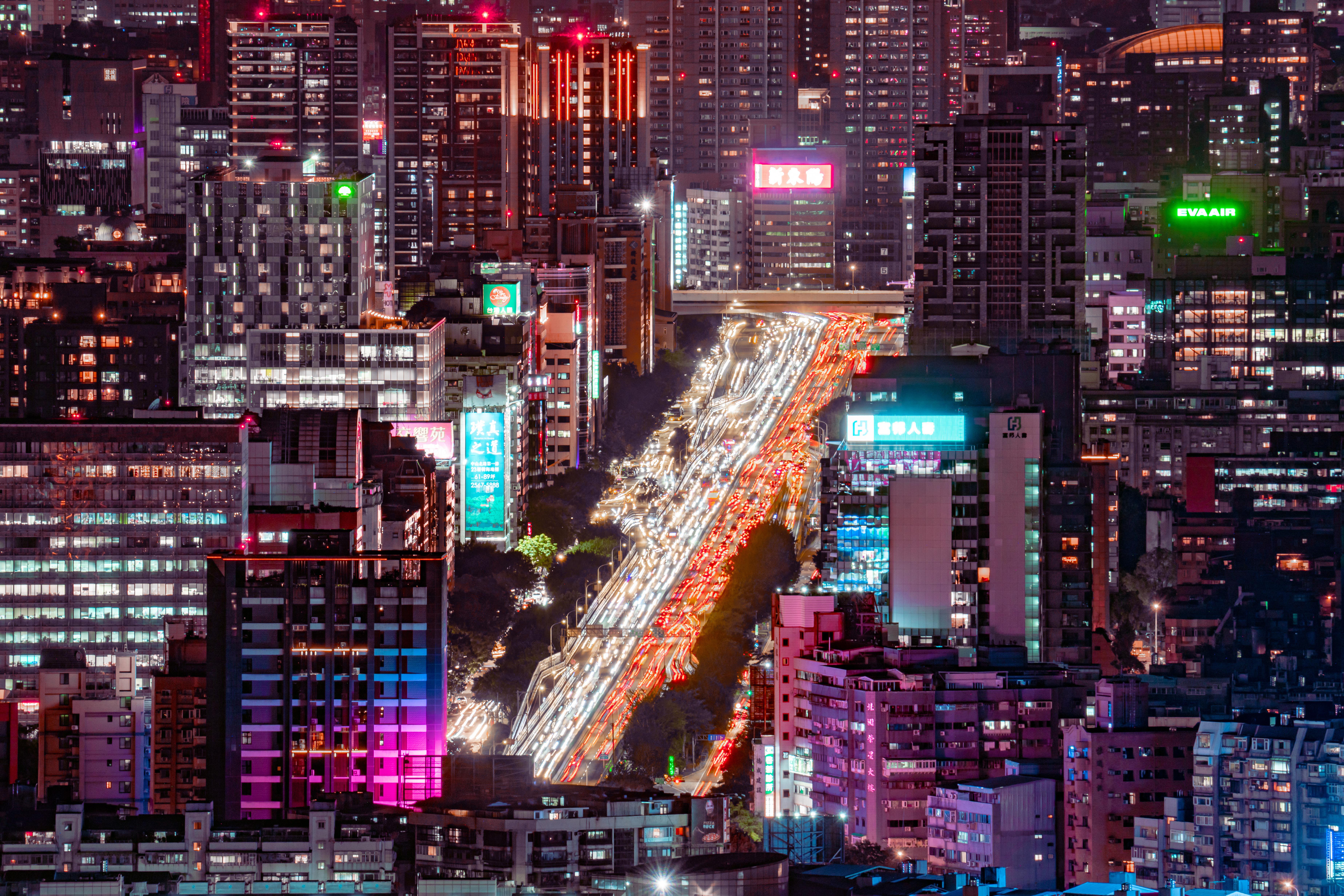 Autopista urbana nocturna con estelas de luces de tránsito entre edificios iluminados